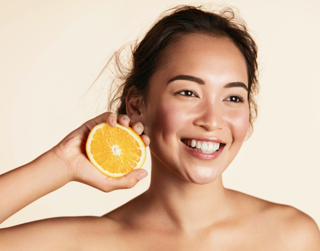 A smmiling woman holding half an orange to her face