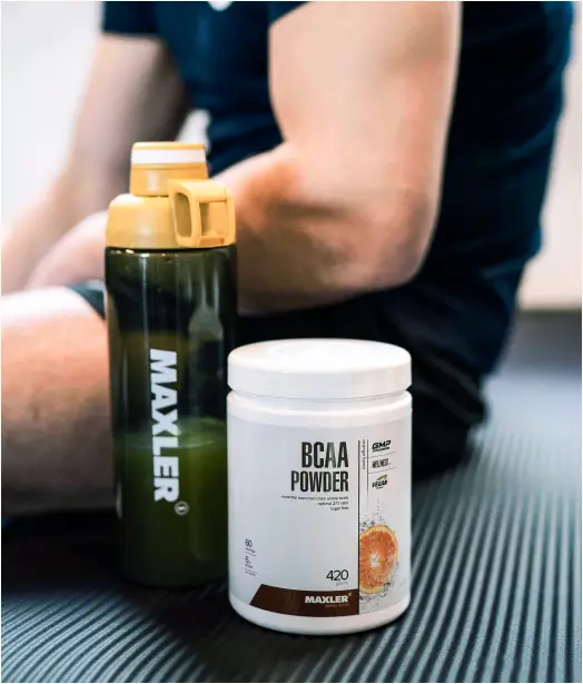 Maxler BCAA Powder and shaker bottle placed on a workout mat next to an athlete after training