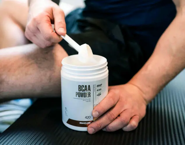 Maxler BCAA Powder and shaker bottle placed on a workout mat next to an athlete after training